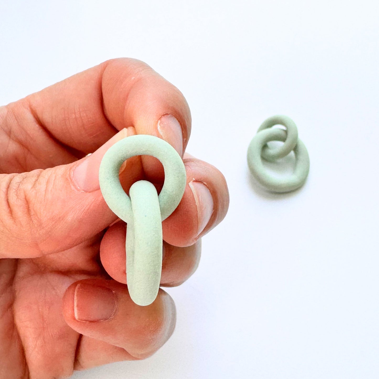 Hand holding a small green clay knot against a white background