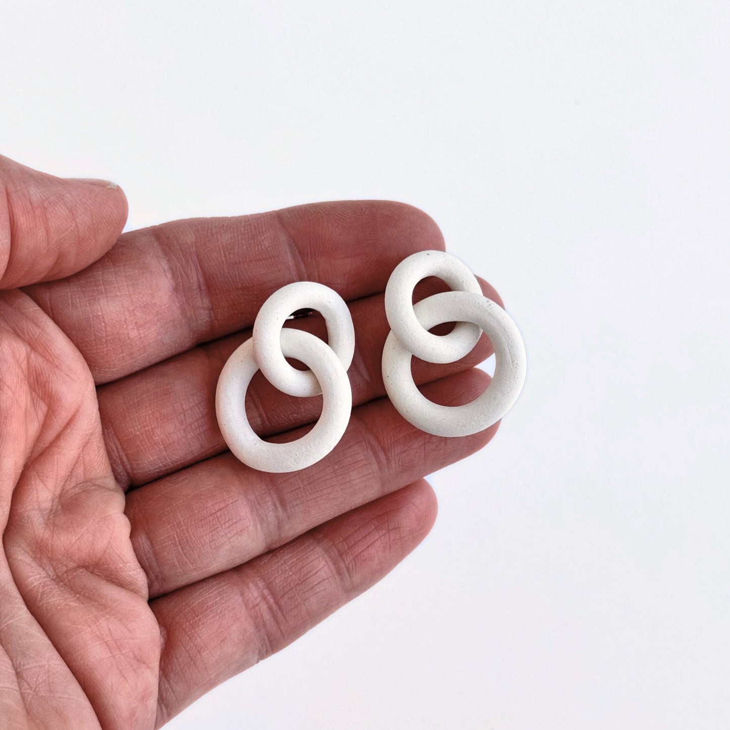 White circular earrings held in a hand against a white background