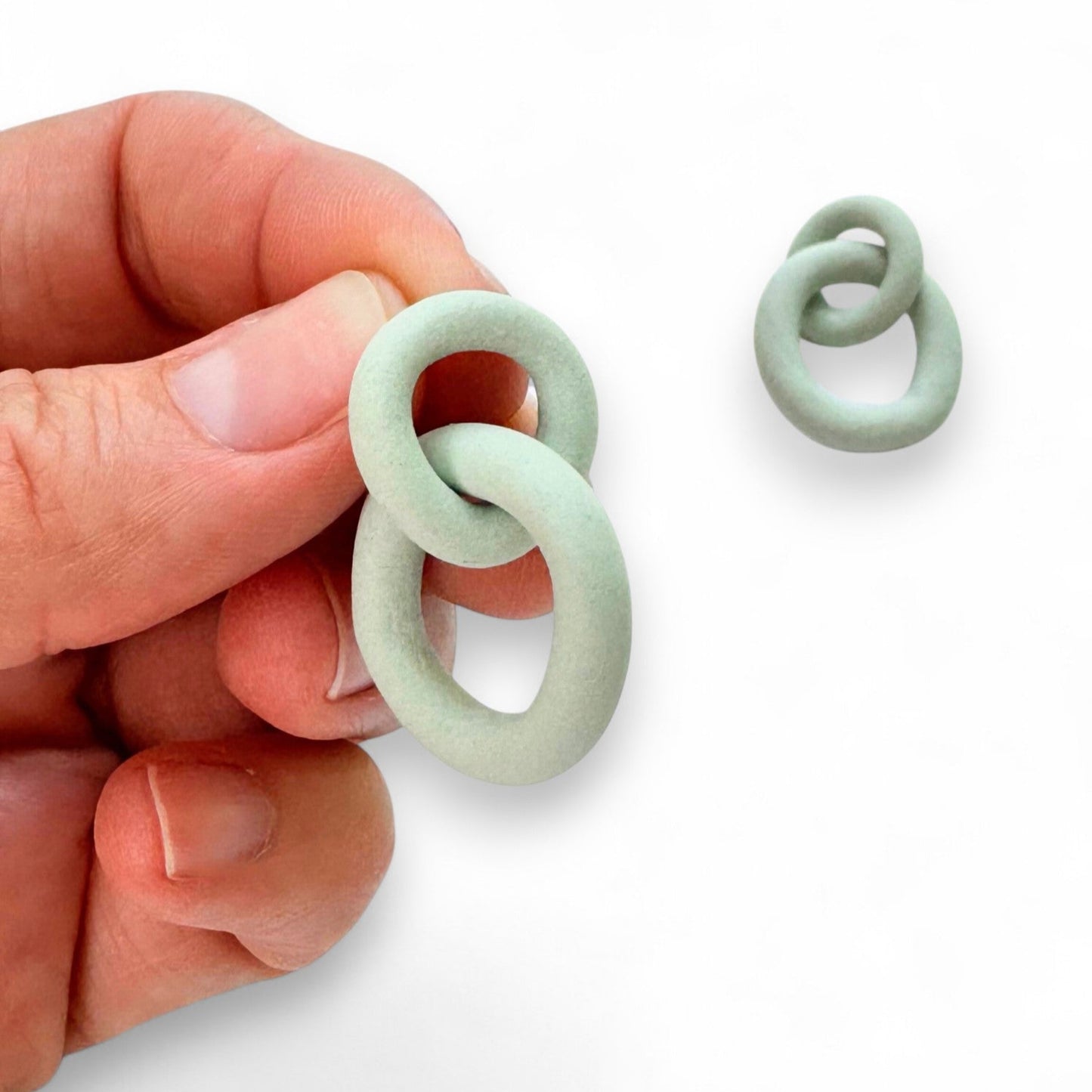 Hand holding a mint green ceramic link against a white background
