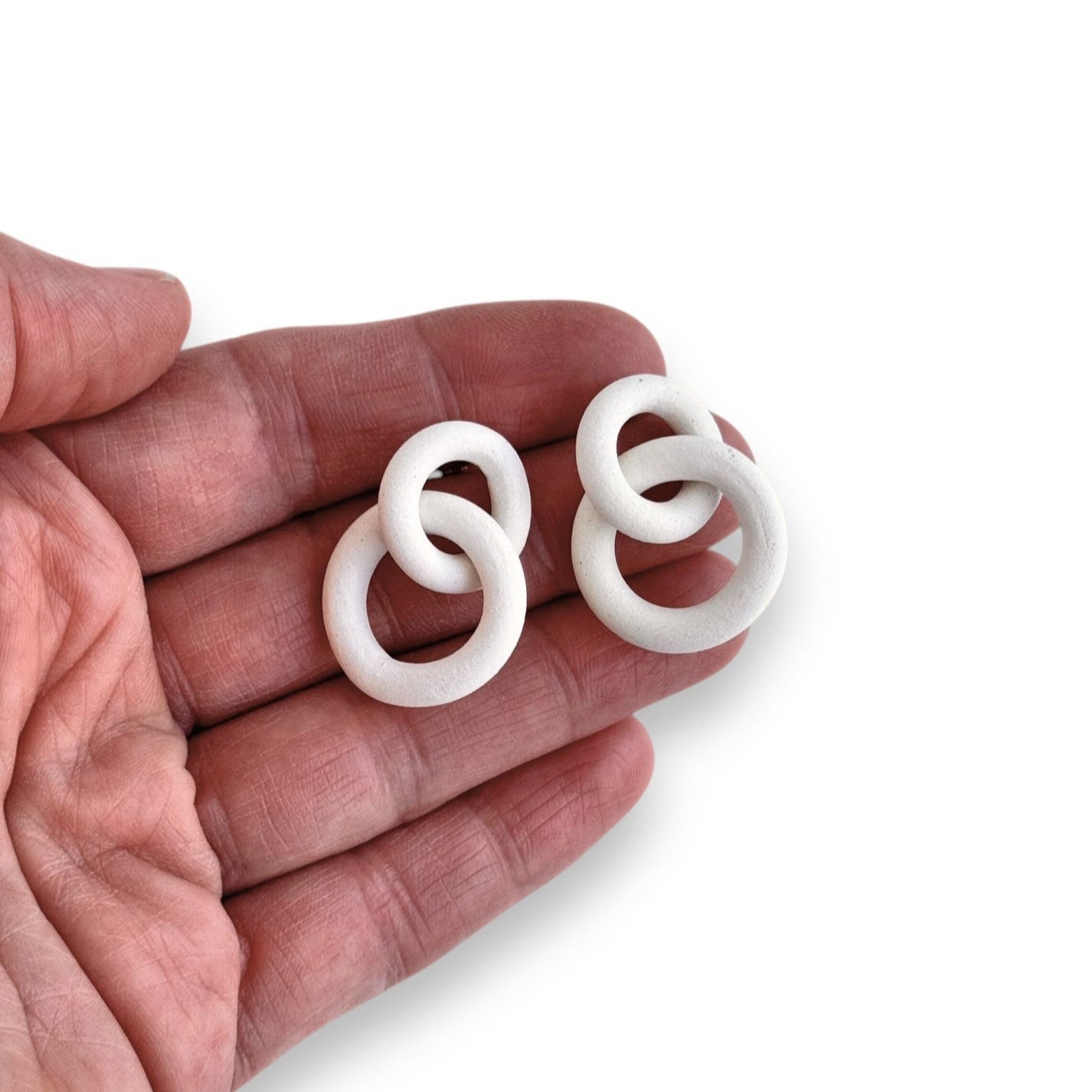 White circular earrings held in a hand against a white background