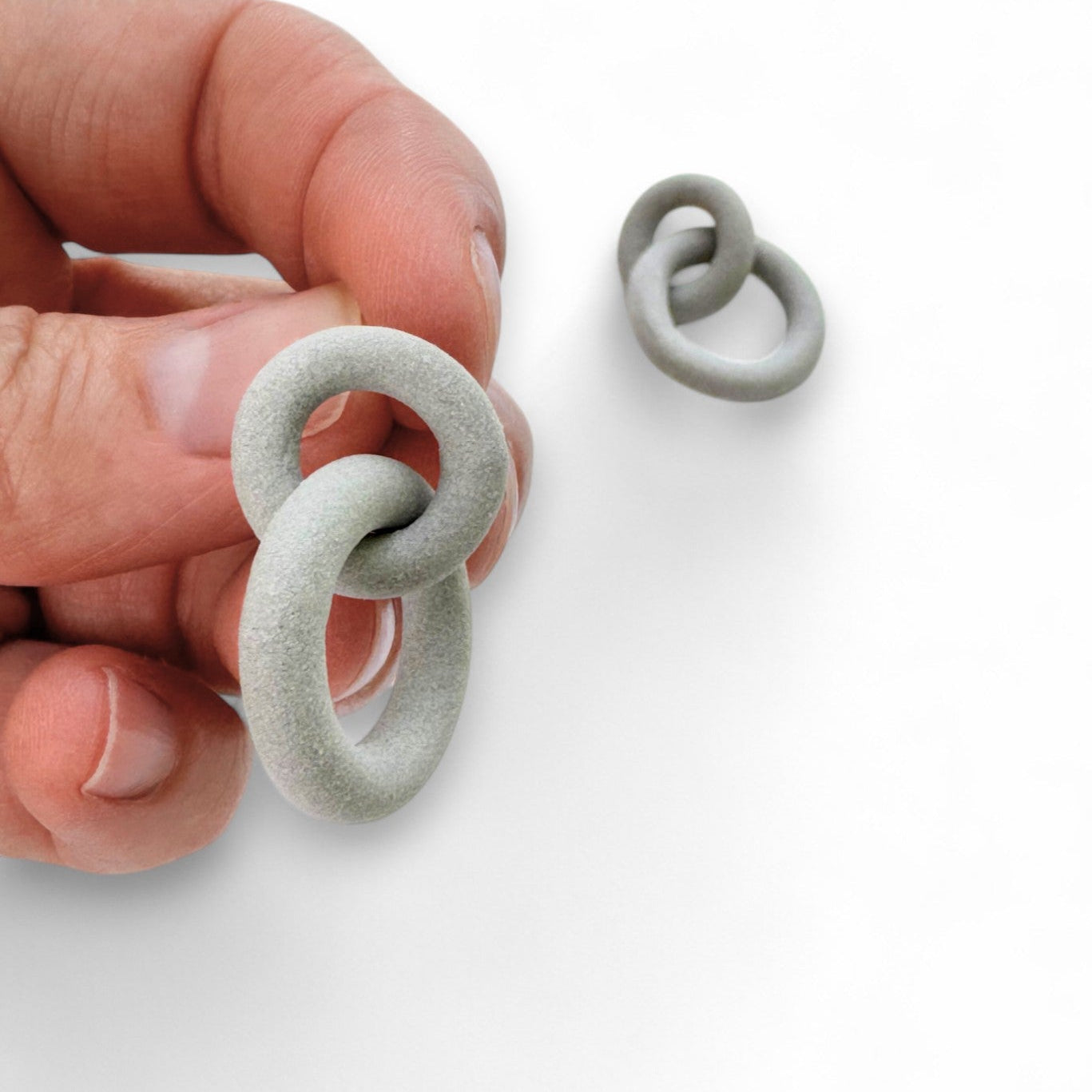 Hand holding a small gray ceramic link against a white background