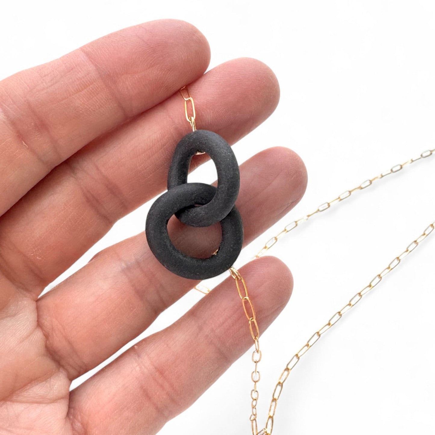 Hand holding a gold chain with a black ceramic pendant against a white background