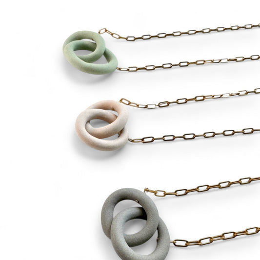 Necklaces with ceramic interlocking rings on gold chains against a white background